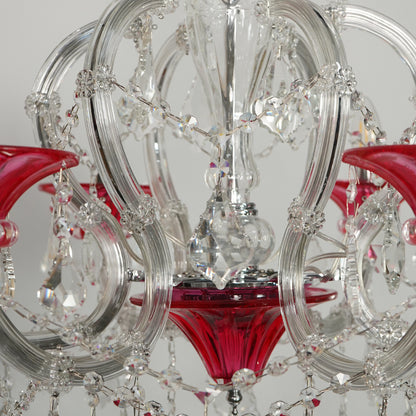 A close-up of a crystal chandelier featuring clear glass rings, hanging faceted crystal beads, and vibrant red glass shades.