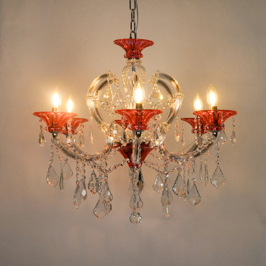 A five-light crystal chandelier with red glass candle-style cups and hanging clear crystal teardrop pendants, shown lit against a plain beige wall.