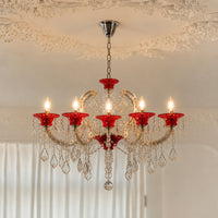 A six-light chandelier with red glass cup holders and clear crystal droplets, hanging from a silver chain in an ornate room with a decorative ceiling.