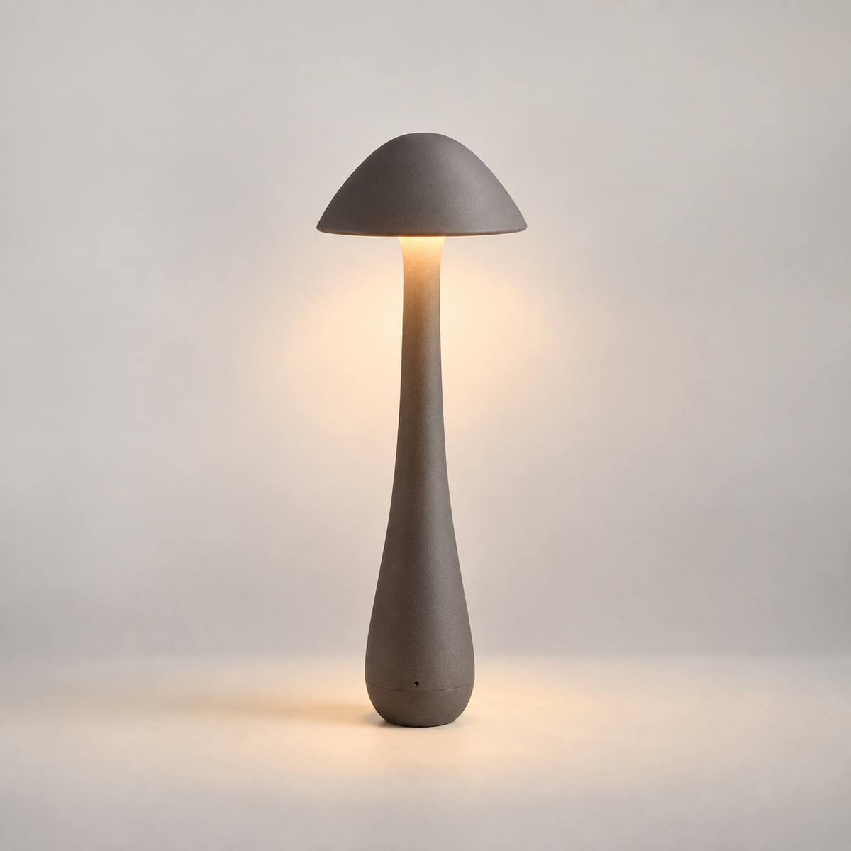 A mushroom-shaped table lamp with a matte gray concrete-like finish, shown lit against a soft neutral background.