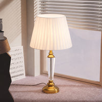 Clear glass table lamp with pleated fabric shade placed on a desk creating warm traditional lighting and decor appeal.