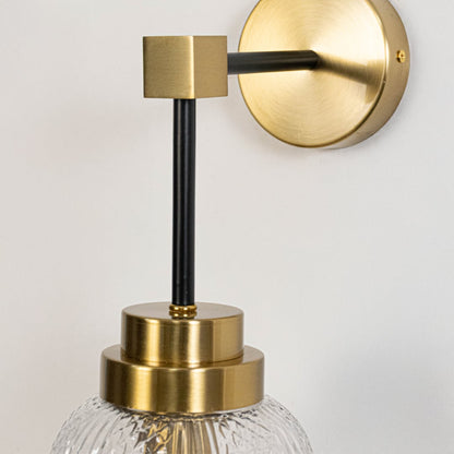 Closeup of luxury gold and black wall sconce with textured glass shade highlighting fine metal frame and premium craftsmanship.