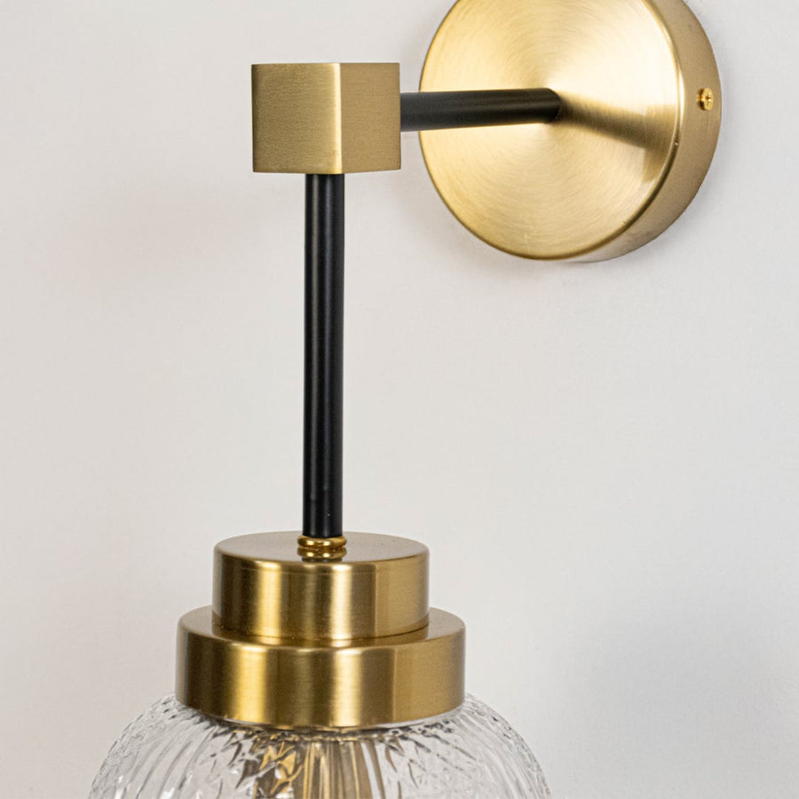 Closeup of luxury gold and black wall sconce with textured glass shade highlighting fine metal frame and premium craftsmanship.