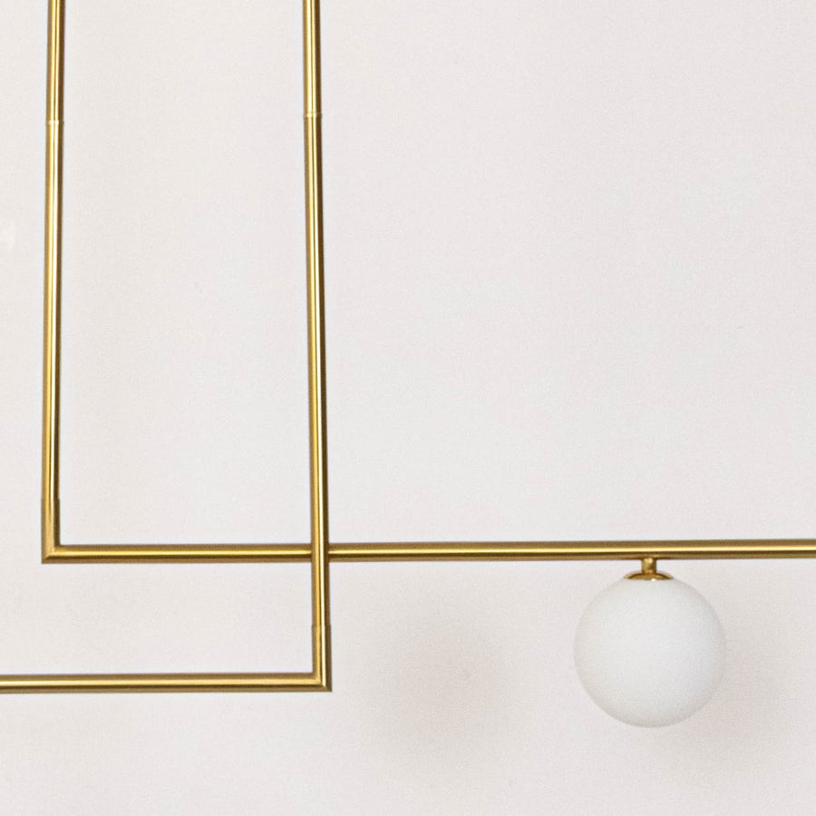 Closeup of gold pendant light with sleek metal frame and round frosted glass globes for modern ceiling lighting design.