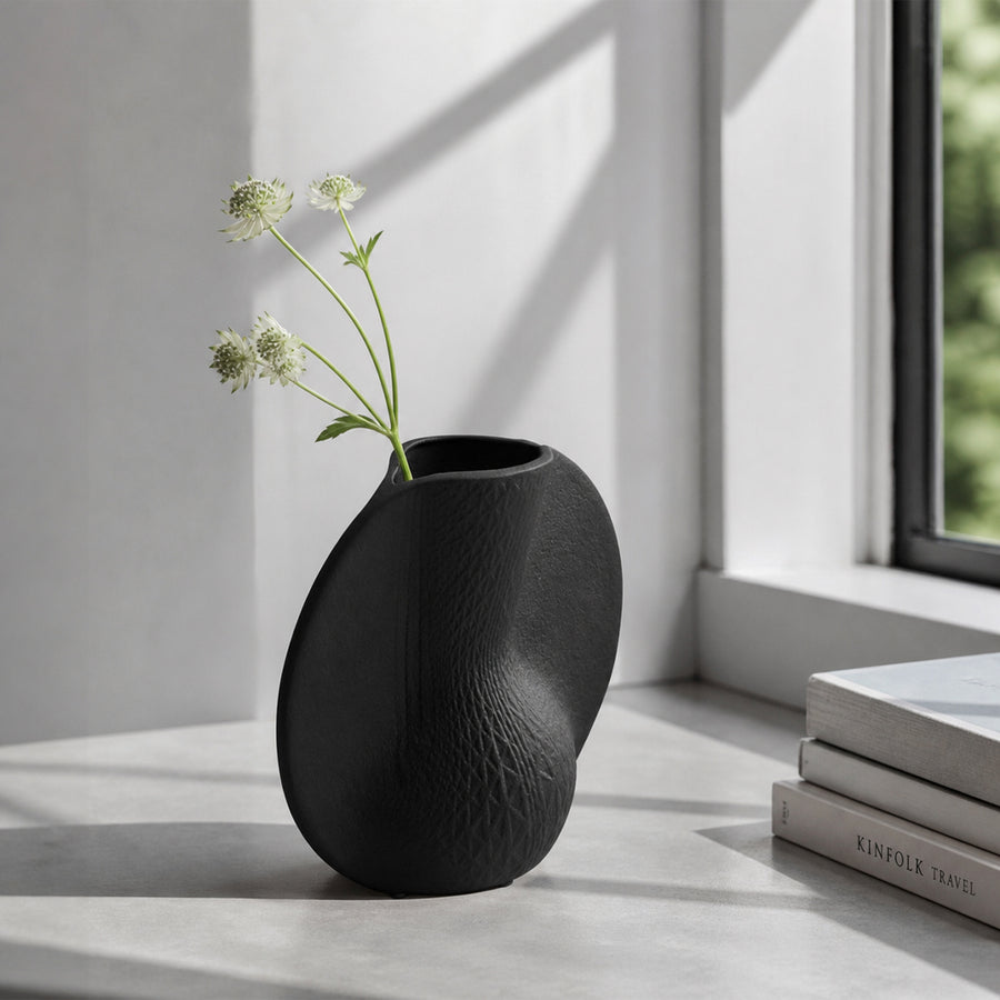 Black textured ceramic flower vase with white blooms placed on marble table for modern home decor styling.