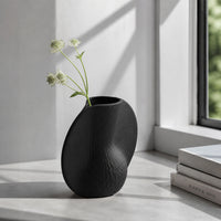 Black textured ceramic flower vase with white blooms placed on marble table for modern home decor styling.
