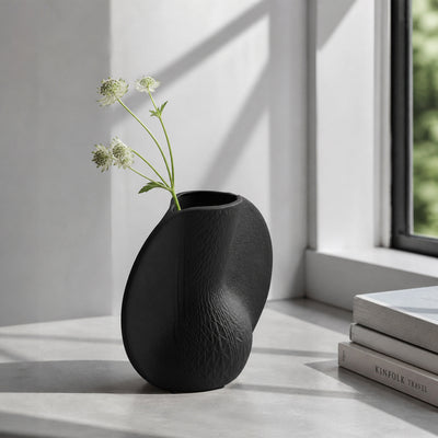 Black textured ceramic flower vase with white blooms placed on marble table for modern home decor styling.