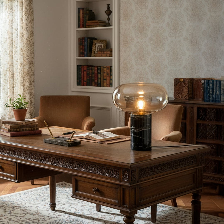 Elegant glass and black marble table lamp glowing warmly on a classic wooden desk creating a cozy vintage study room ambience.