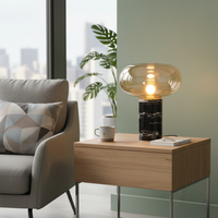 Amber glass table lamp with black marble base placed on a wooden side table creating warm modern ambient lighting indoors.