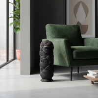 Decorative floor vase crafted in black textured material placed beside green armchair adding modern accent and depth to living room decor.