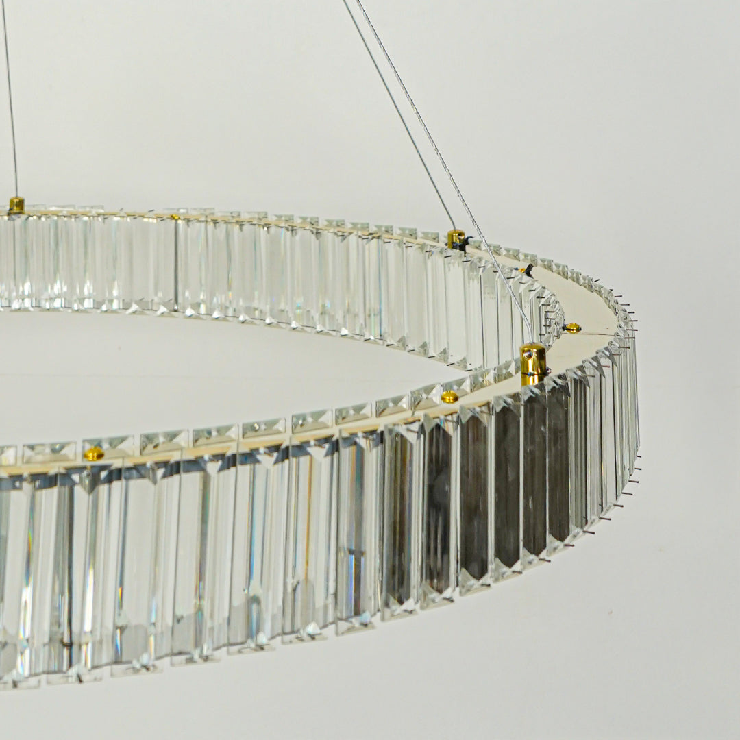 Close up modern crystal ring chandelier with gold metal frame and hanging glass prisms against clean white ceiling background for luxury lighting.
