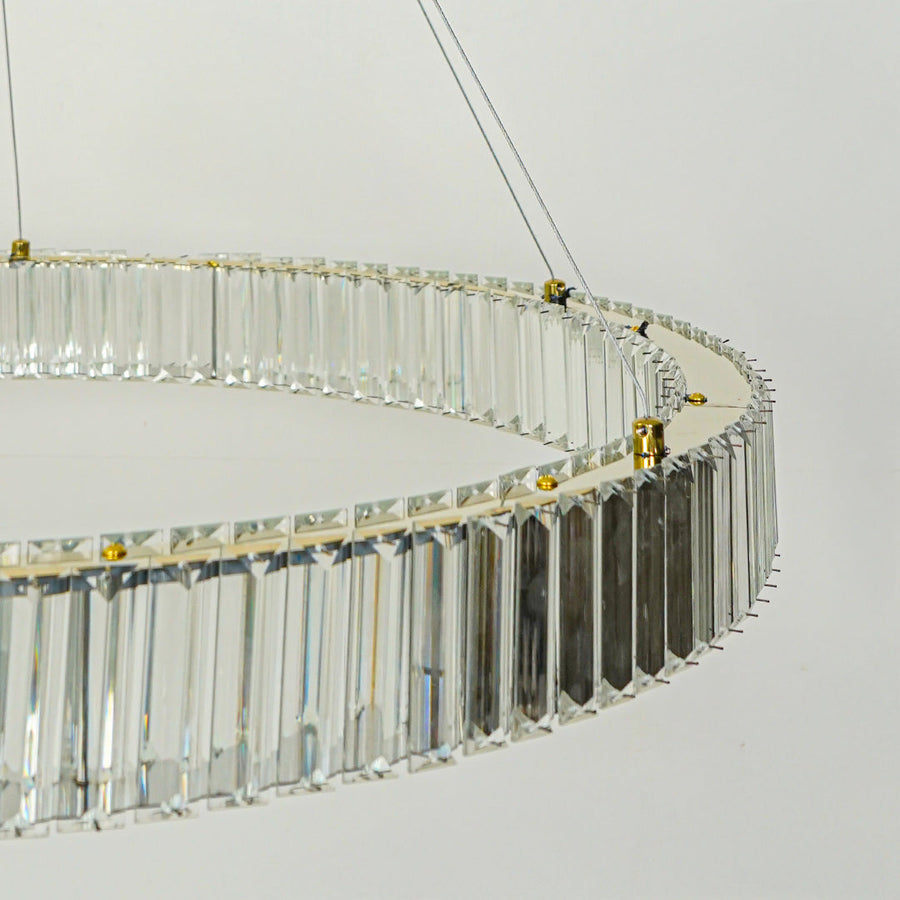 Close up modern crystal ring chandelier with gold metal frame and hanging glass prisms against clean white ceiling background for luxury lighting.