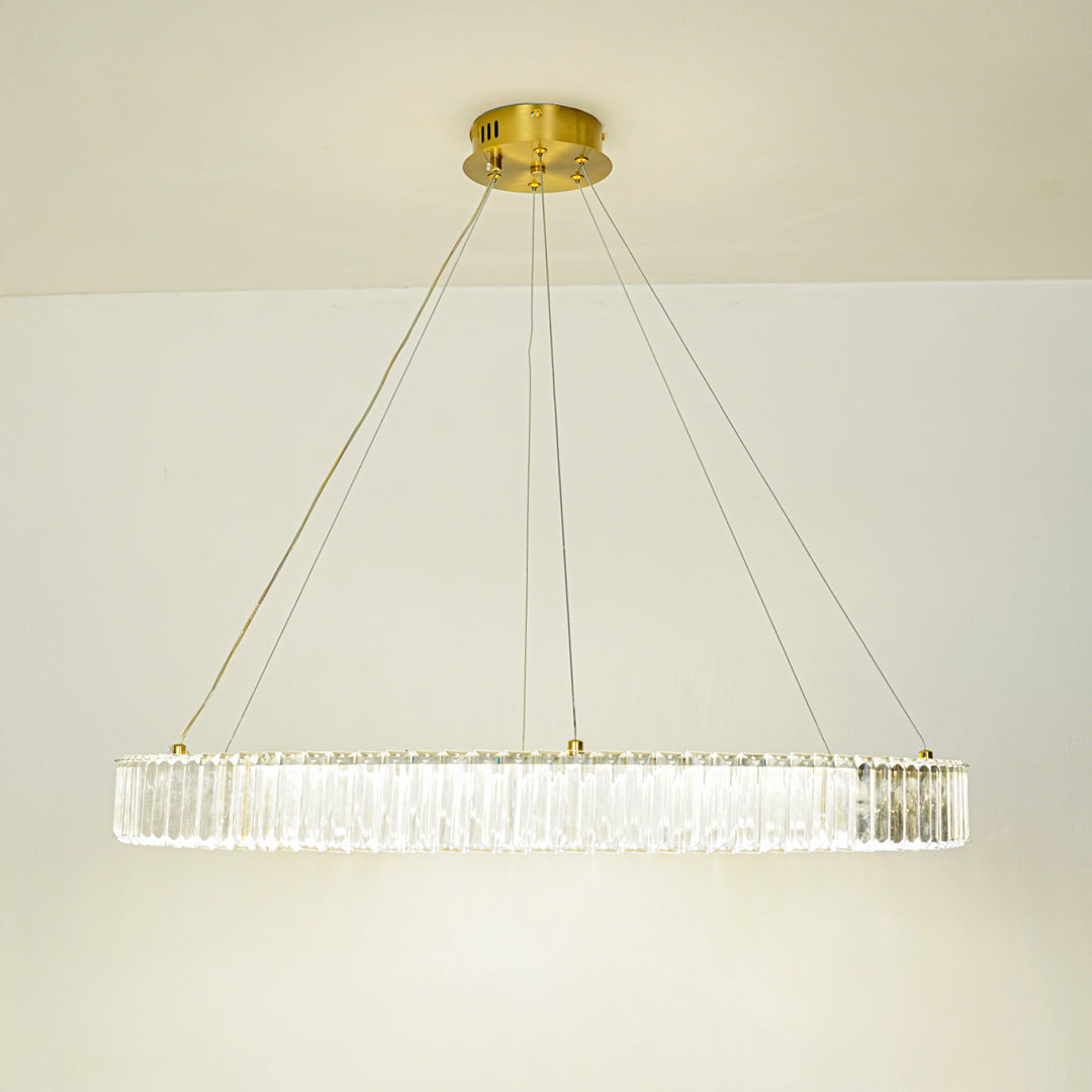Contemporary linear crystal pendant light with gold metal frame suspended against clean white ceiling background ideal for modern dining or living space lighting.
