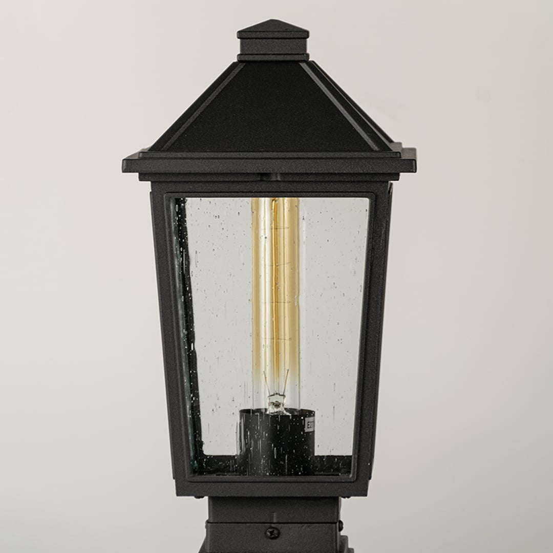 Black outdoor post light Closeup Image showing ribbed glass panels and warm exposed filament bulb.