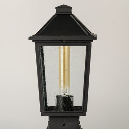 Black outdoor post light Closeup Image showing ribbed glass panels and warm exposed filament bulb.