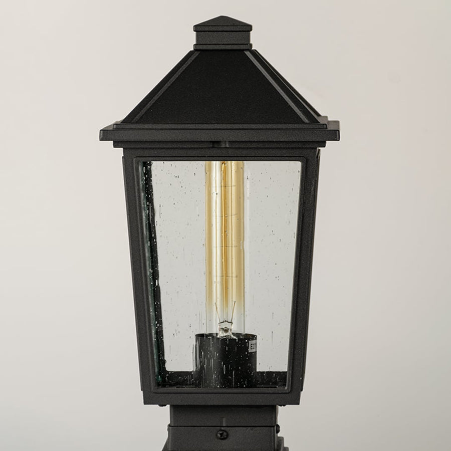 Black outdoor post light Closeup Image showing ribbed glass panels and warm exposed filament bulb.