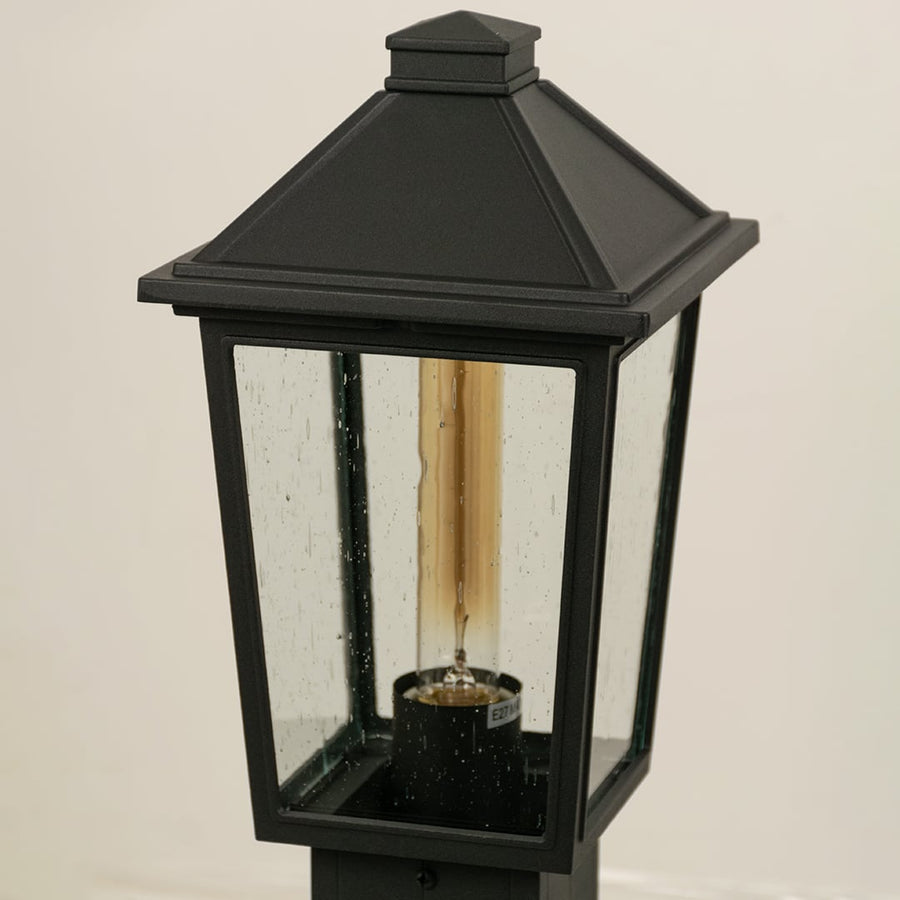 A detailed closeup of the outdoor post light showing the textured clear glass and metal frame with visible bulb socket and refined craftsmanship.