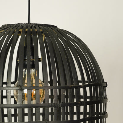 A close-up of a black woven rattan or wicker birdcage-style pendant light with a visible warm-toned Edison bulb inside, hanging against a plain light background.
