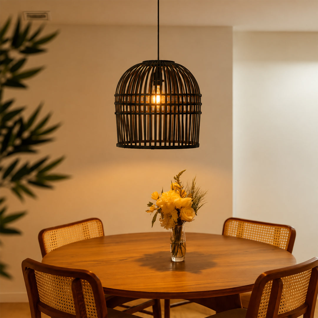 A black metal cage pendant light hangs above a round wooden dining table with four woven-back chairs. A glass vase with yellow flowers sits on the table, and warm sunlight streams in from the side against a beige wall.