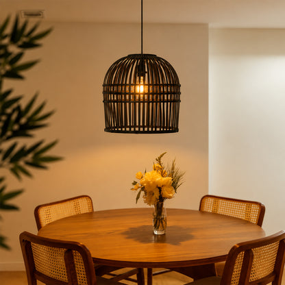 A black metal cage pendant light hangs above a round wooden dining table with four woven-back chairs. A glass vase with yellow flowers sits on the table, and warm sunlight streams in from the side against a beige wall.