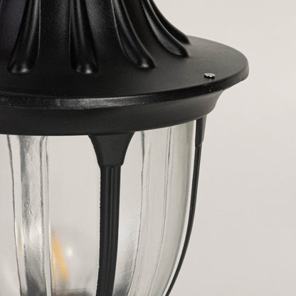Closeup of decorative outdoor black pillar lamp with dome top and transparent glass panels highlighting classic design.