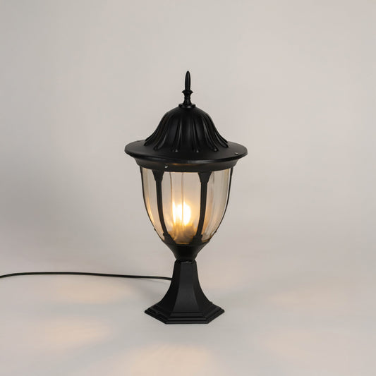 Black metal outdoor gate light with glowing bulb and clear glass shade for modern decor use.