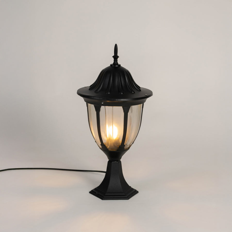 Black metal outdoor gate light with glowing bulb and clear glass shade for modern decor use.