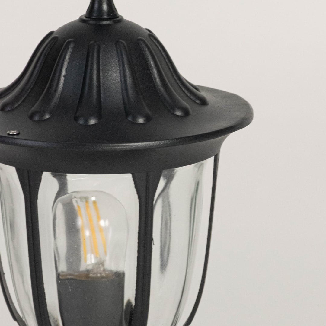 Closeup of black pillar lamp with decorative top and glass shade highlighting elegant outdoor garden and gate lighting design.