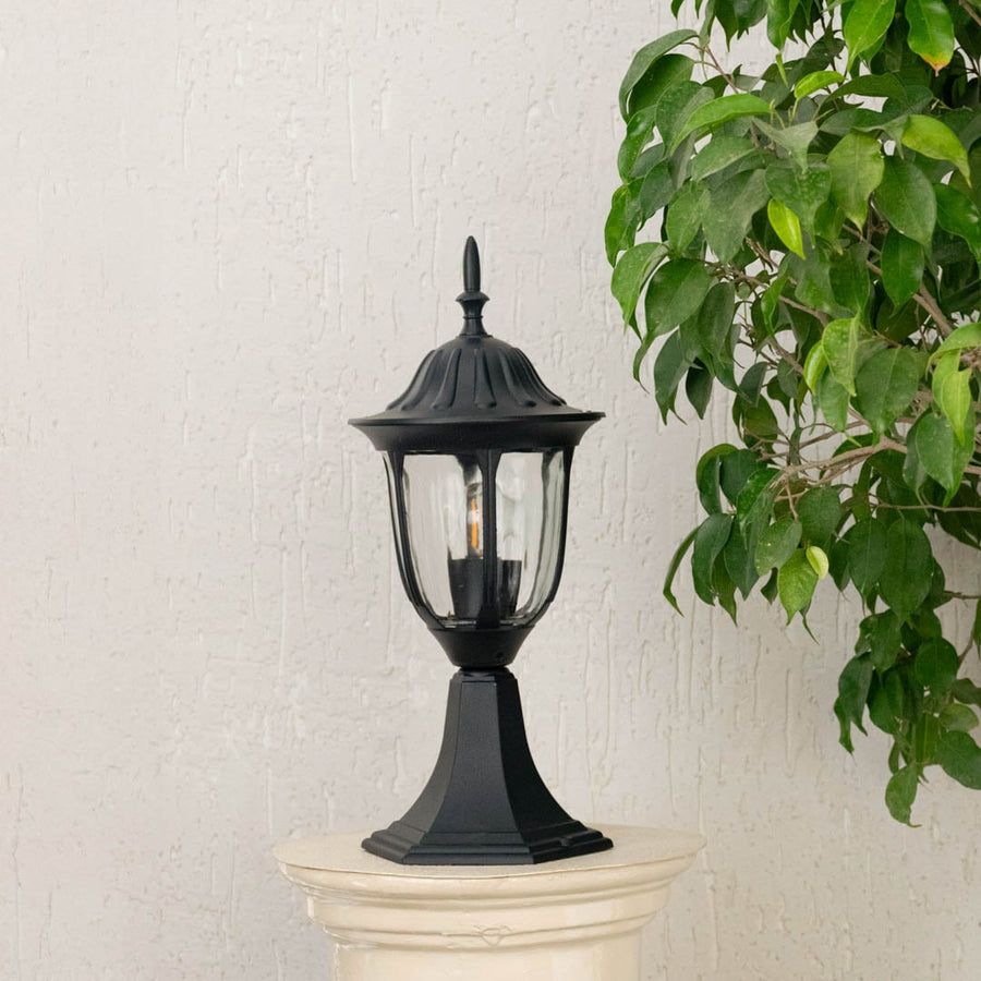 Outdoor pillar lantern with black metal body placed on white pillar shown unlit adding classic architectural accent to exterior decor.