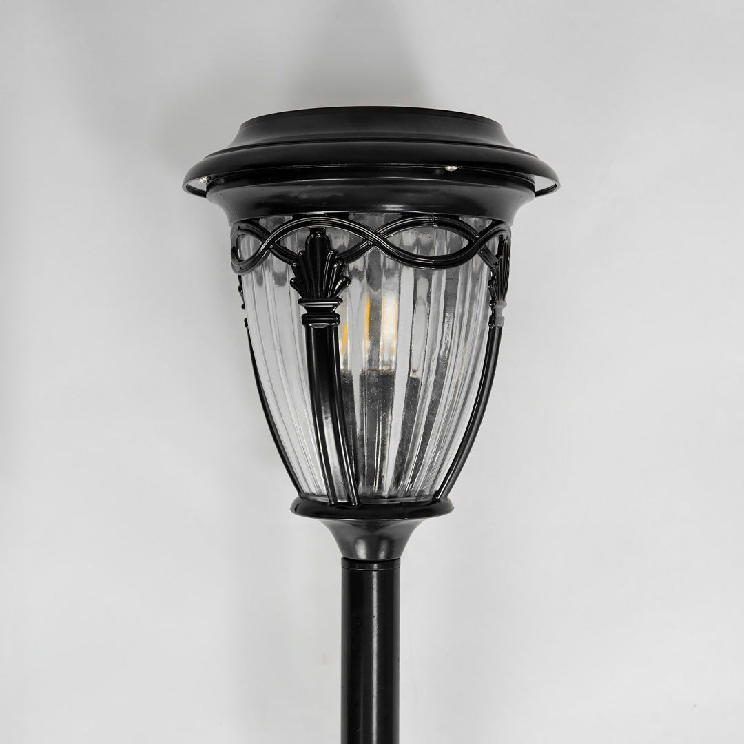 Closeup of black metal solar garden pathway light with clear glass shade for outdoor landscape lighting display.