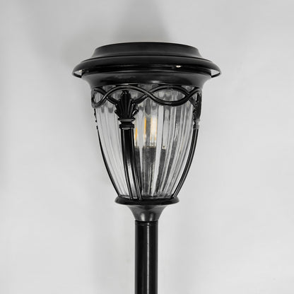 Closeup of black metal solar garden pathway light with clear glass shade for outdoor landscape lighting display.