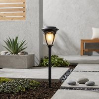 Modern black iron tapered solar post lantern light fixture on mulch bed next to concrete patio pavers for backyard styling.