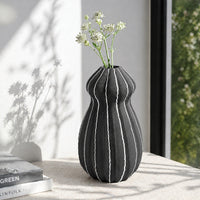 Black textured ceramic flower vase with white blooms placed on marble table for modern home decor styling.