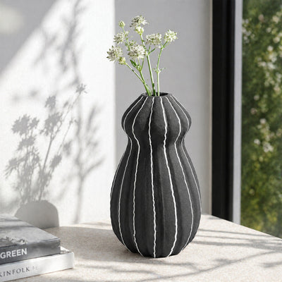 Black textured ceramic flower vase with white blooms placed on marble table for modern home decor styling.