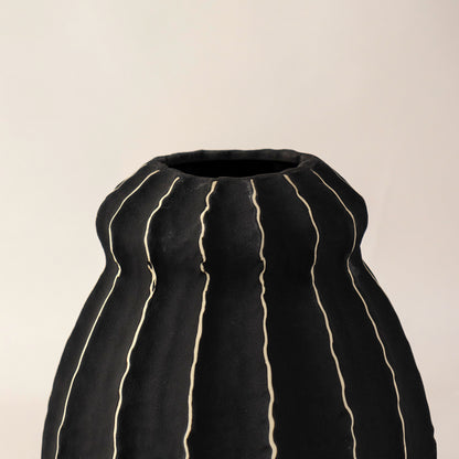 Black ceramic vase with vertical gold stripe accents placed on white surface against neutral background enhancing luxury contemporary home decor appeal.