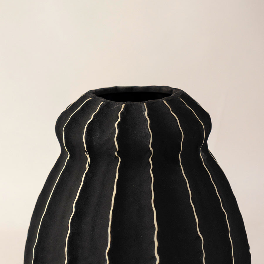 Black ceramic vase with vertical gold stripe accents placed on white surface against neutral background enhancing luxury contemporary home decor appeal.