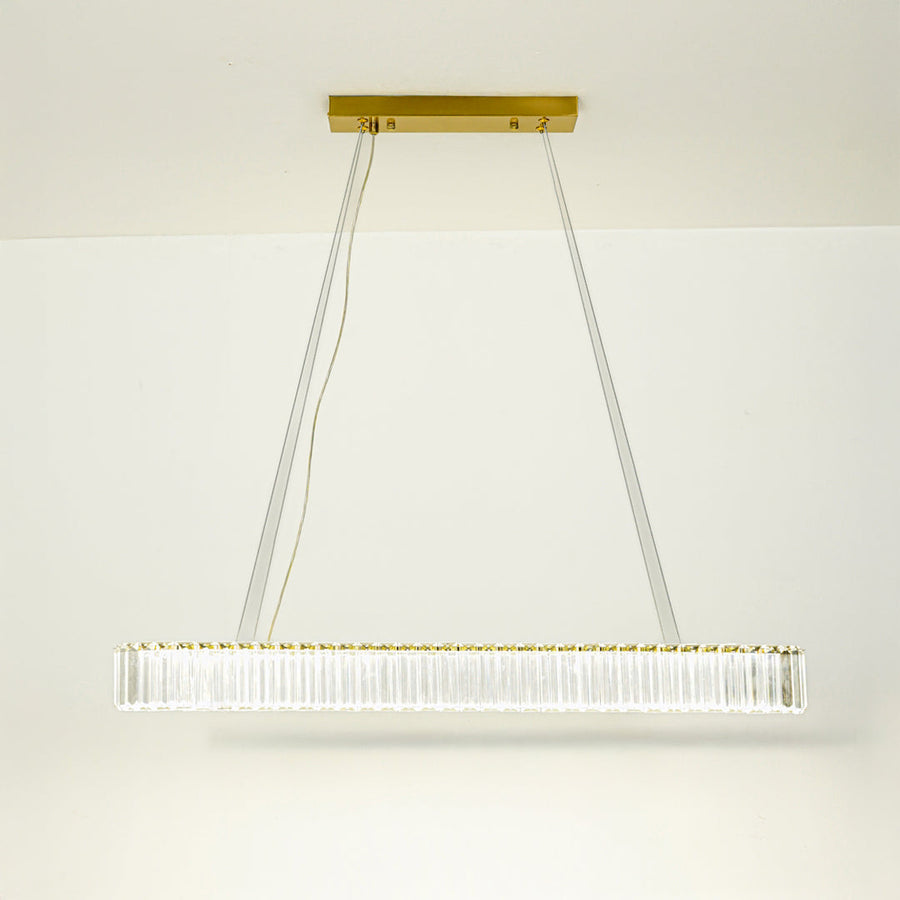 Elegant long bar pendant light with gold metal finish suspended on cables against neutral wall background ideal for luxury interior decor lighting.
