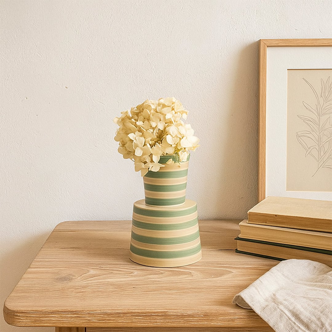 A modern striped ceramic vase in green and beige tones displayed in a soft minimal setting  adding a fresh decorative touch to any space.