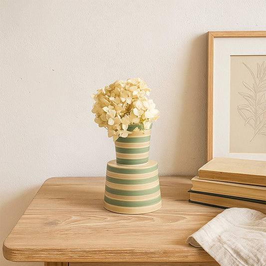 A modern striped ceramic vase in green and beige tones displayed in a soft minimal setting  adding a fresh decorative touch to any space.