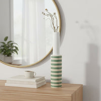 A tall striped decorative vase displayed in natural sunlight on a minimal white surface creating a clean lifestyle look with soft shadows and a modern aesthetic.