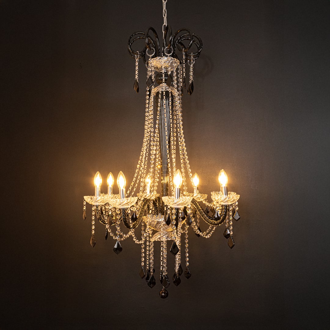 Tall black and clear crystal chandelier glowing softly on black background creating a dramatic luxury ceiling feature.