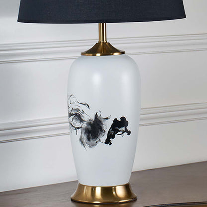 Closeup of white ceramic lamp with flowing black abstract artwork gold base and textured black shade highlighting its artistic modern craftsmanship.