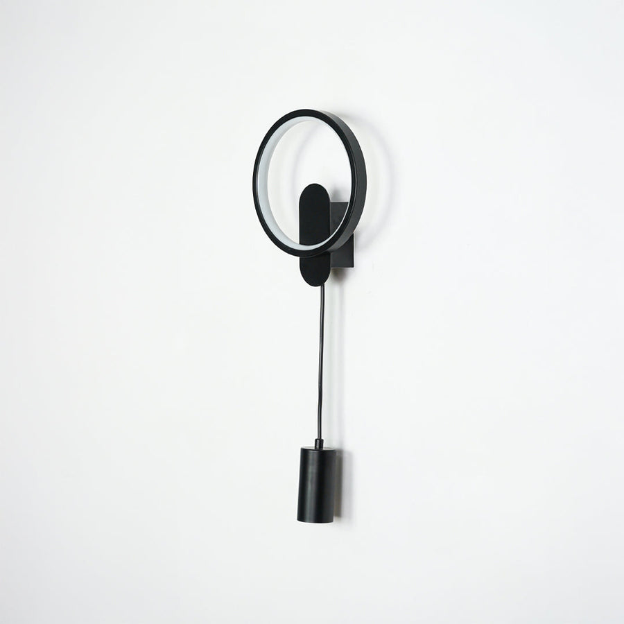 Black wall light with circular LED ring and cylindrical spotlight mounted on neutral wall background ideal for modern bedroom or hallway lighting.