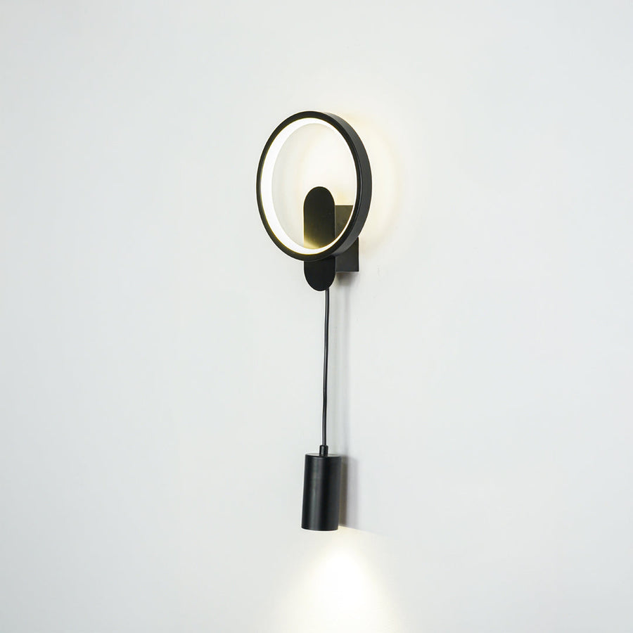 Contemporary gold wall sconce with LED ring and black spotlight mounted on neutral wall background ideal for modern bedroom or hallway lighting.

