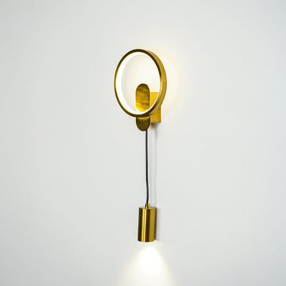 Minimal gold wall sconce with round frame and cylindrical spotlight shade on clean neutral wall background perfect for contemporary interior lighting.