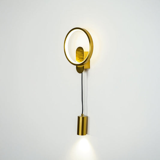 Minimal gold wall sconce with round frame and cylindrical spotlight shade on clean neutral wall background perfect for contemporary interior lighting.
