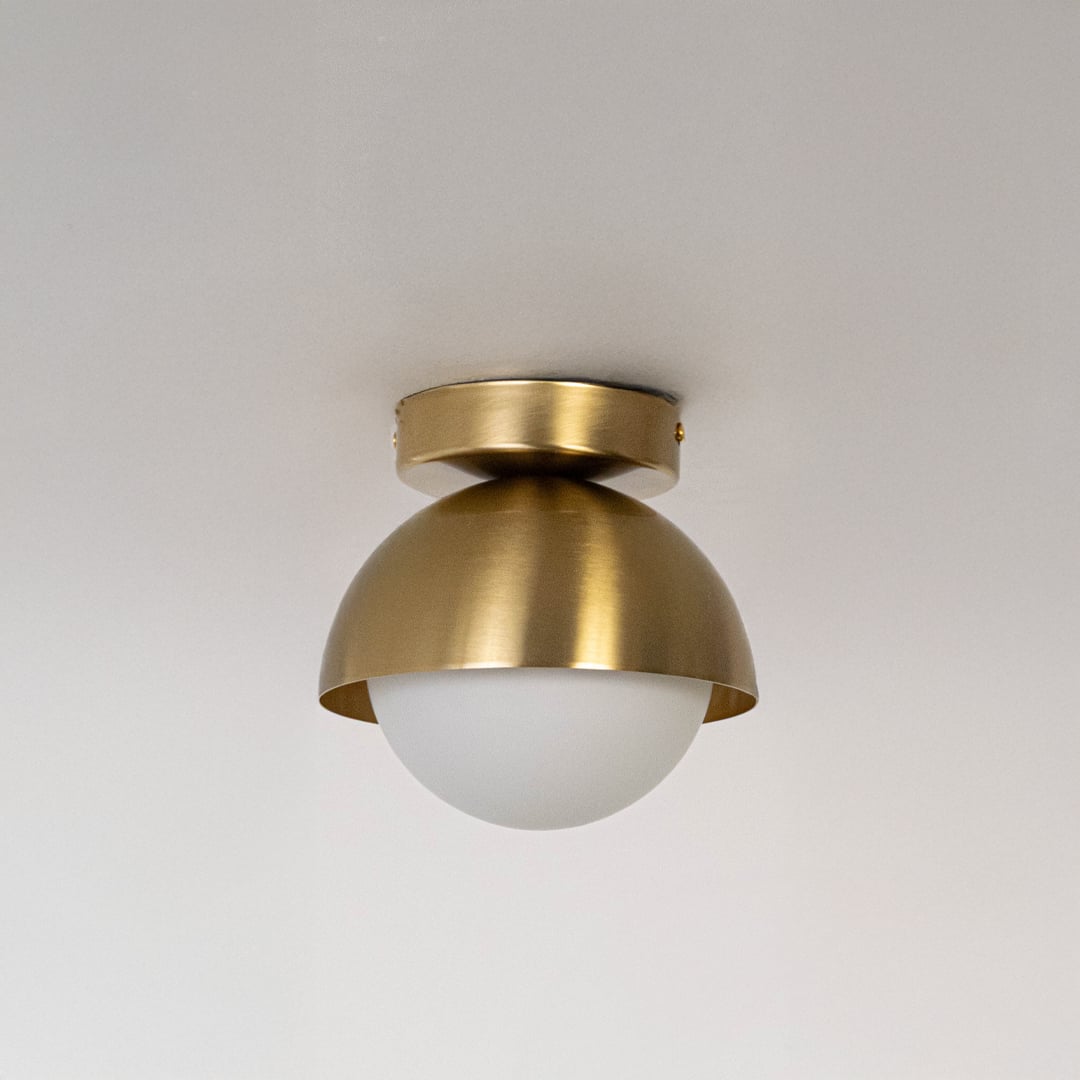 Ceiling light with gold dome shade and frosted white glass globe shown switched off on white background.
