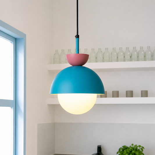 A modern pendant light with a matte turquoise blue dome shade, a dusty pink bowl accent, and a glowing white globe bulb, hanging in a bright kitchen setting.