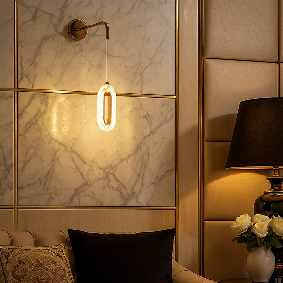 Gold metal wall mounted pendant light glowing warmly on marble accent wall beside bed adding luxury ambient lighting to modern bedroom decor.
