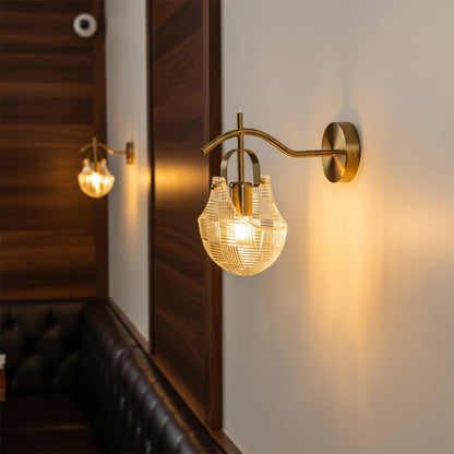 Luxury gold wall sconce light fixture with a textured glass shade casting a warm glow over a restaurant booth seat.
